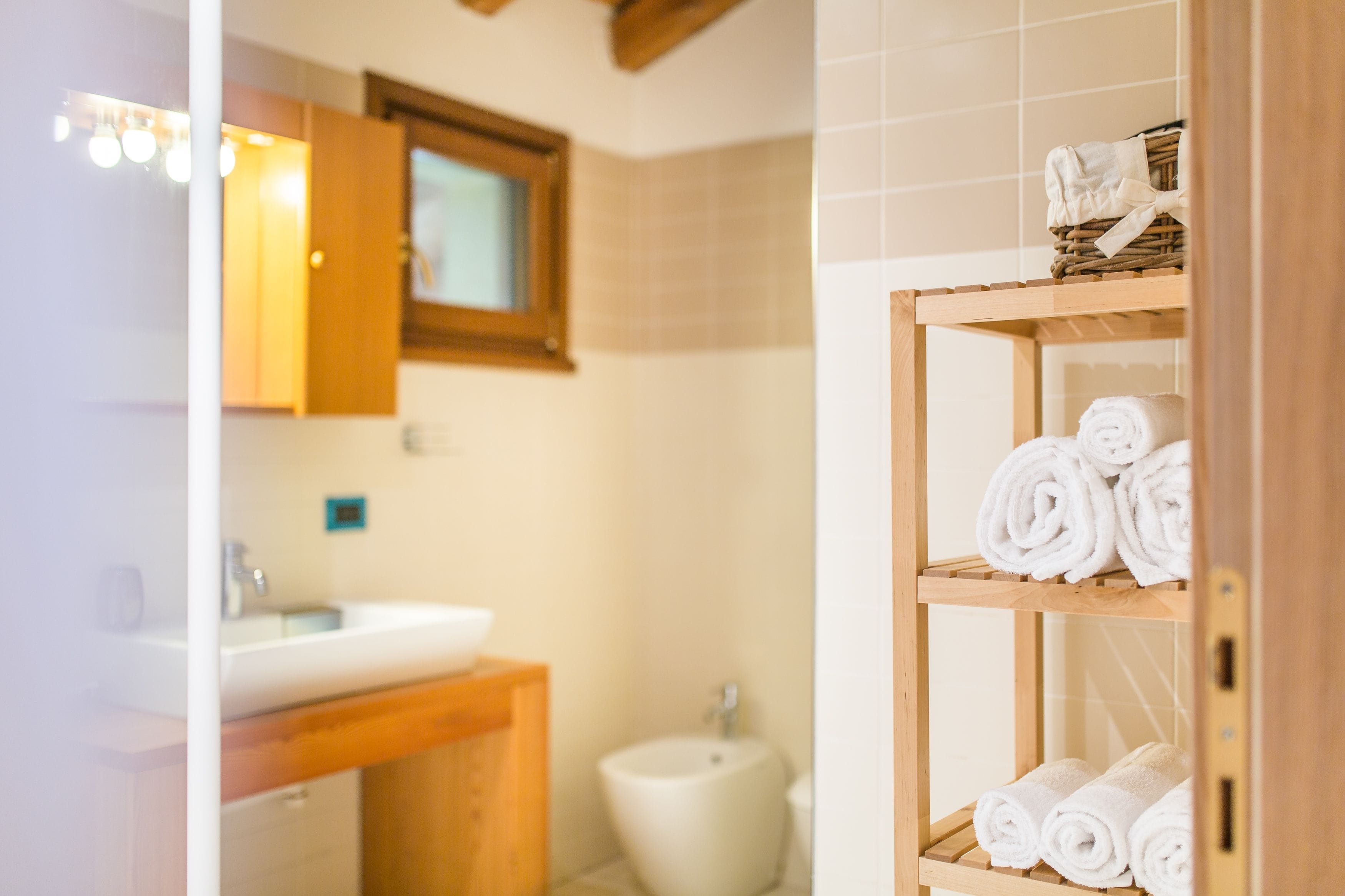 Un bany amb un moble de tocador de fusta, un lavabo, un vàter i una estant amb tovalloles enrere.