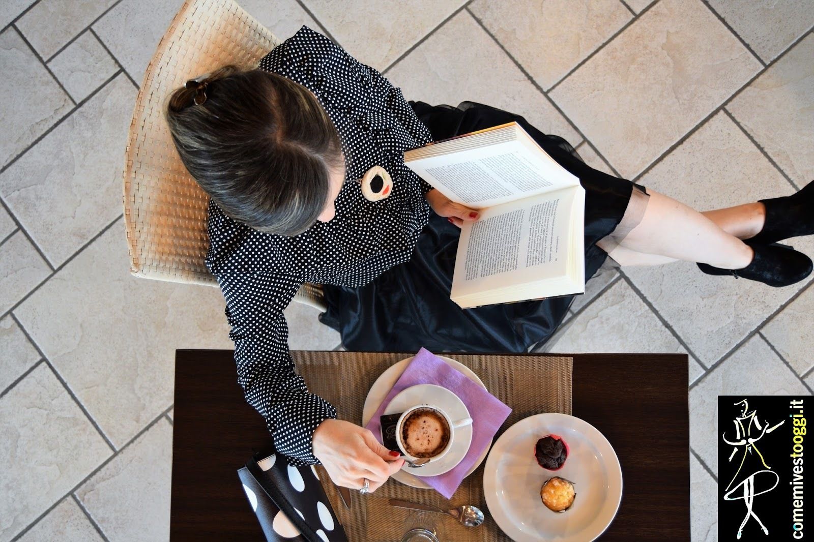 Eine Person liest ein Buch an einem Tisch, neben einer Tasse Kaffee und einem Dessertteller.