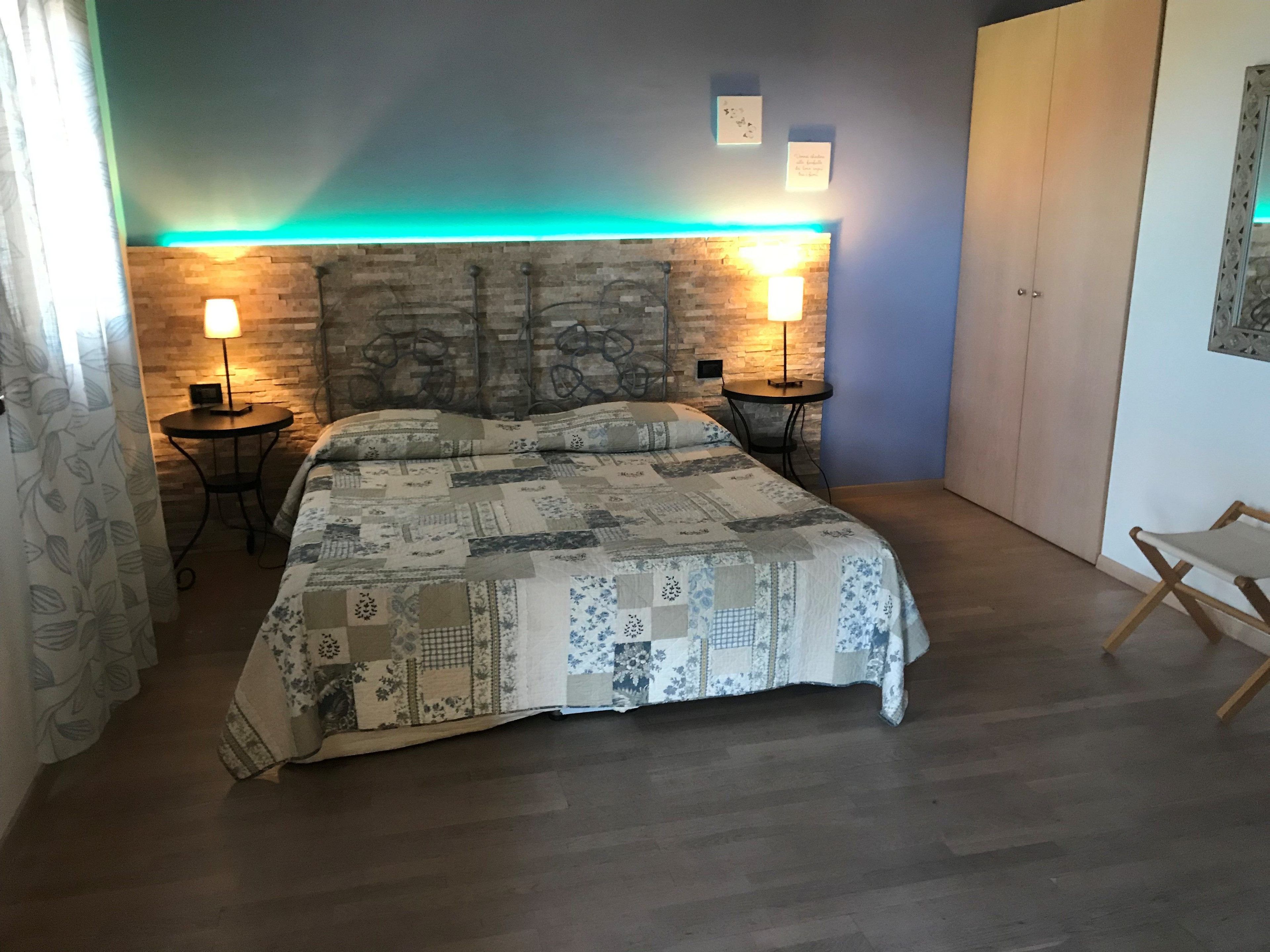 A bedroom with a stone-patterned headboard, two bedside tables with lamps, a bed with a patchwork quilt, and a wooden floor.