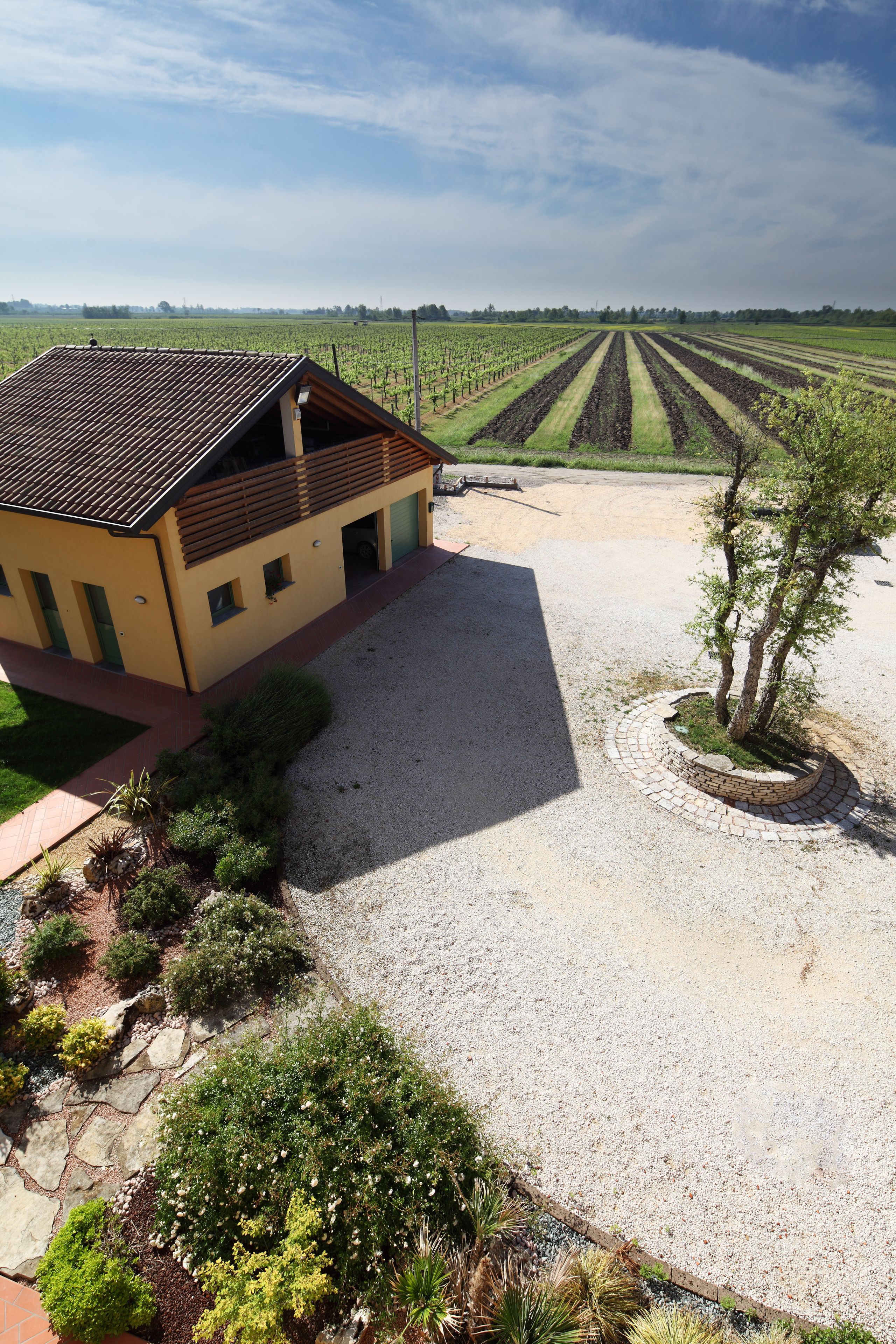 A building with a tiled roof, a gravel driveway, and a landscaped area with shrubs and a tree.