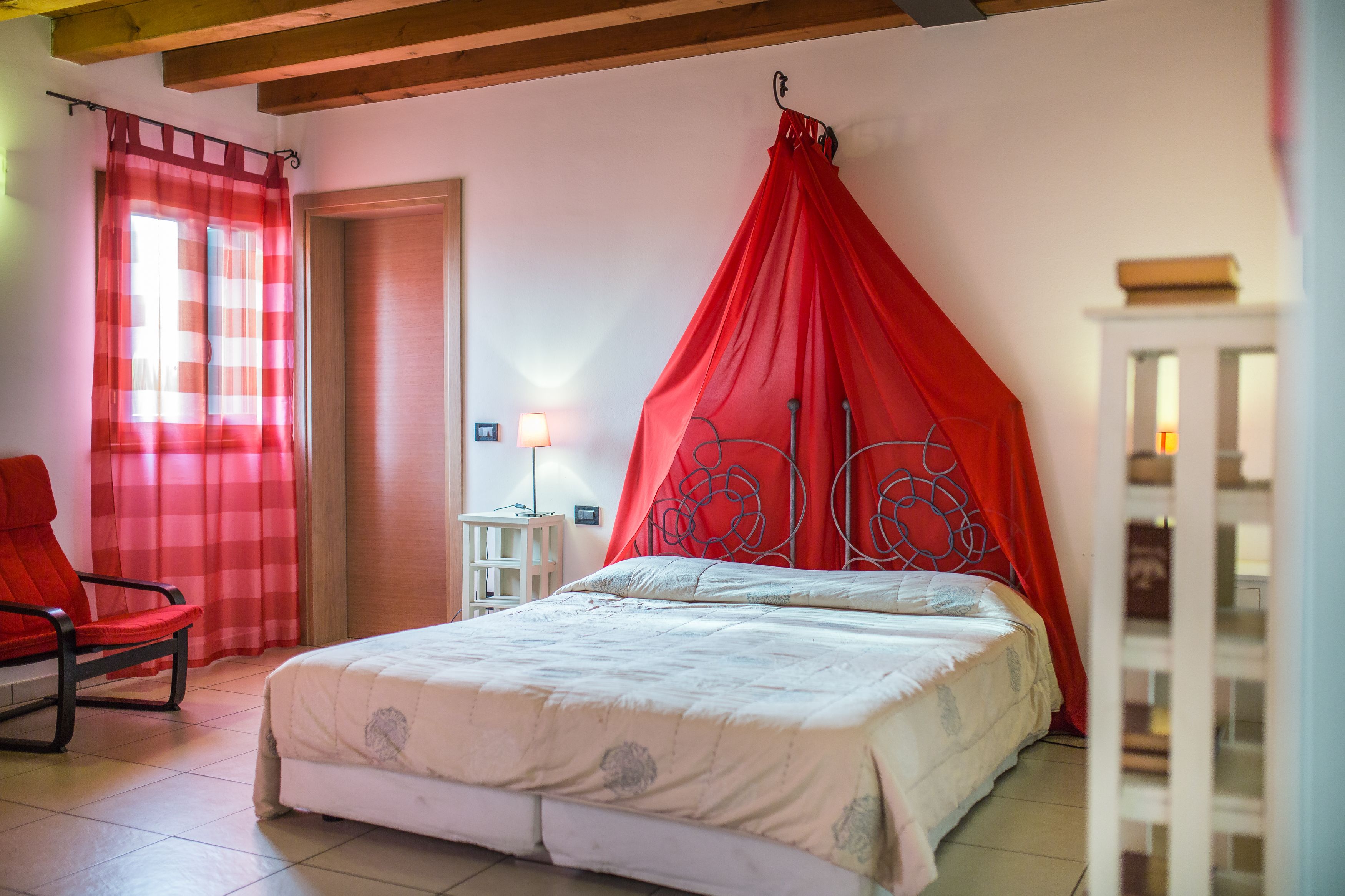 Un dormitorio con cama, una silla roja, una mesita de noche y una lámpara.