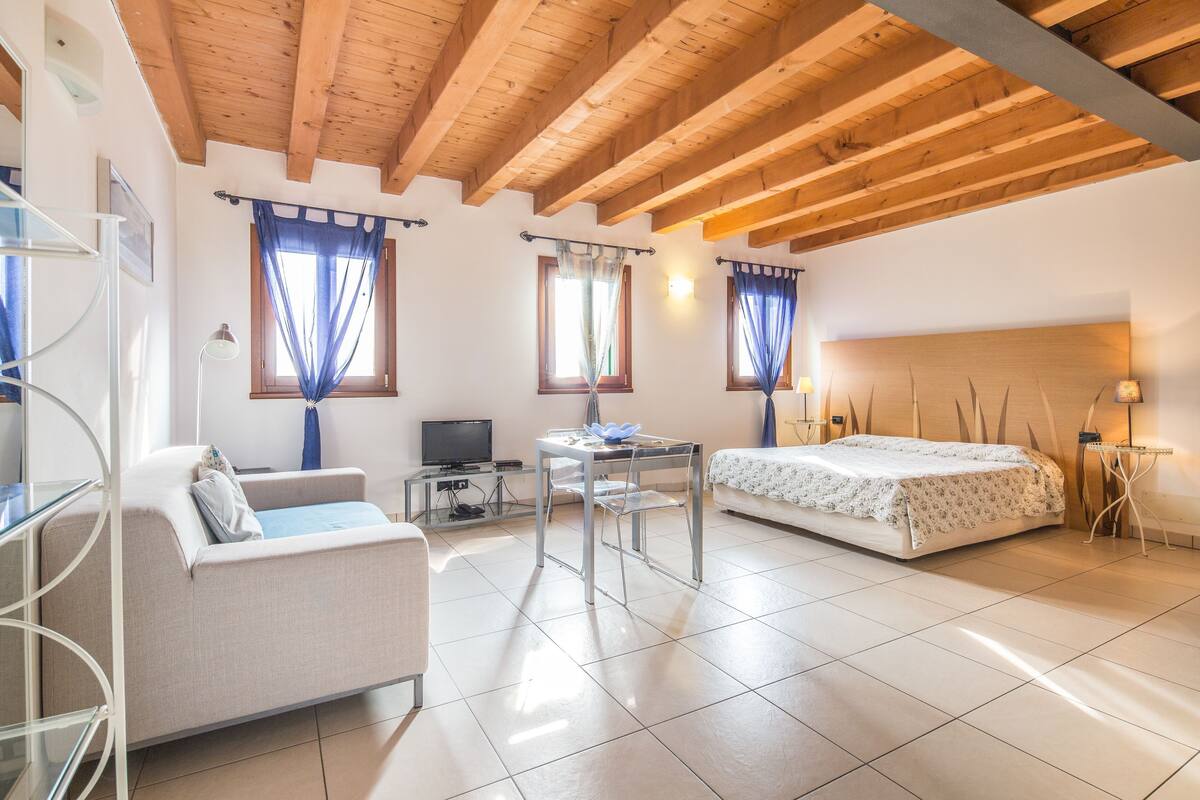 Une pièce comprenant un lit, un canapé, une table, un téléviseur et une fenêtre avec des rideaux.