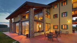 A modern two-story building with a covered patio area, large windows, and outdoor seating. - TENUTA AGANIS (Palazzolo dello Stella)