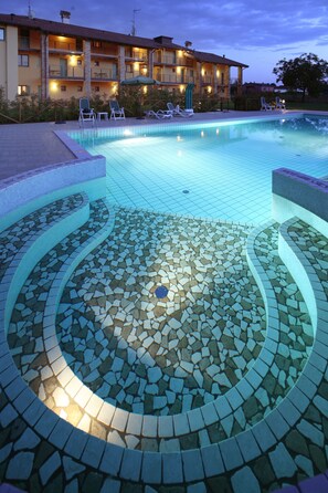 A swimming pool with a mosaic tile design, surrounded by lounge chairs and a building with balconies.