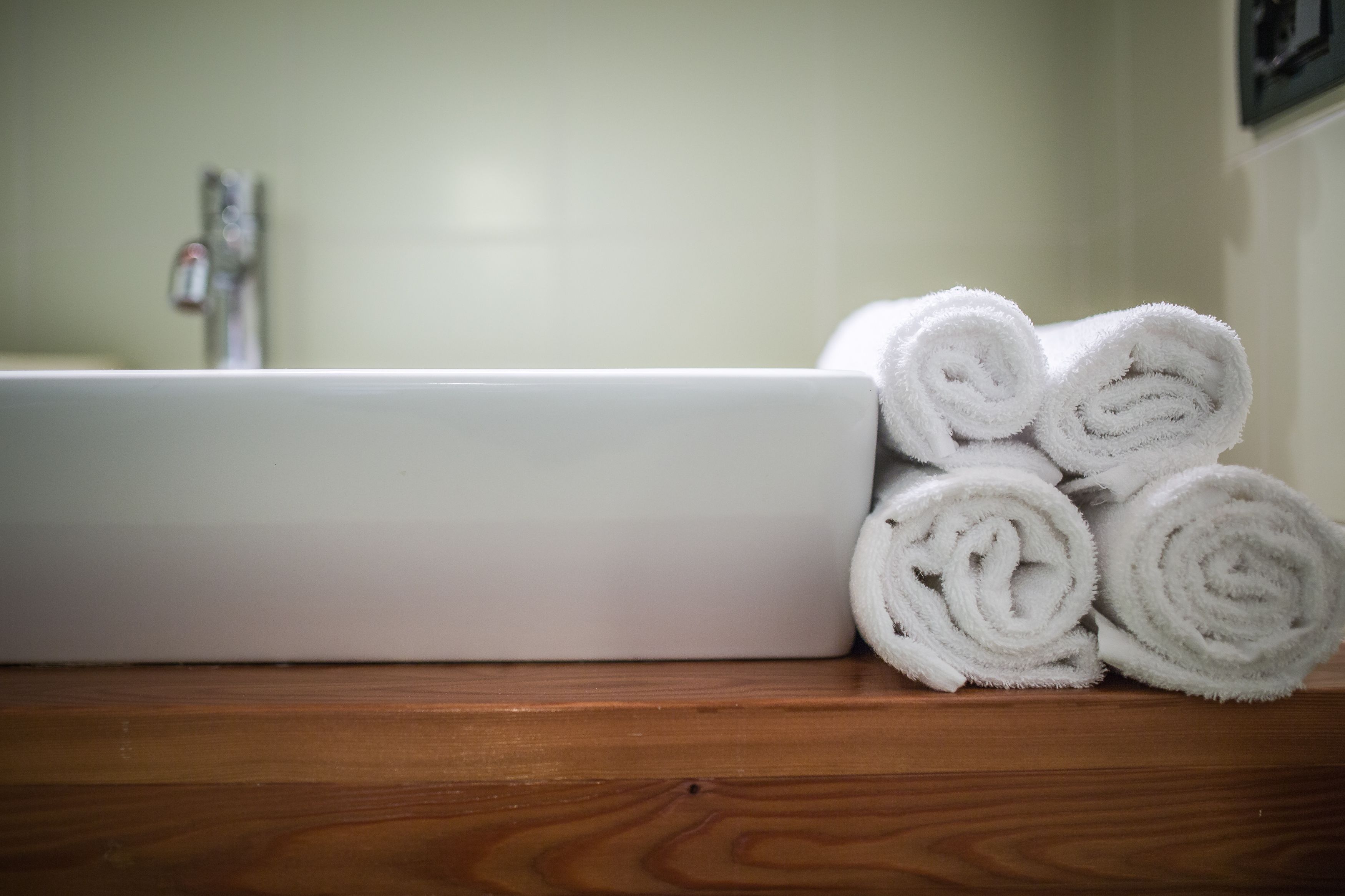 A bathroom with a white bathtub and several rolled white towels on a wooden surface.