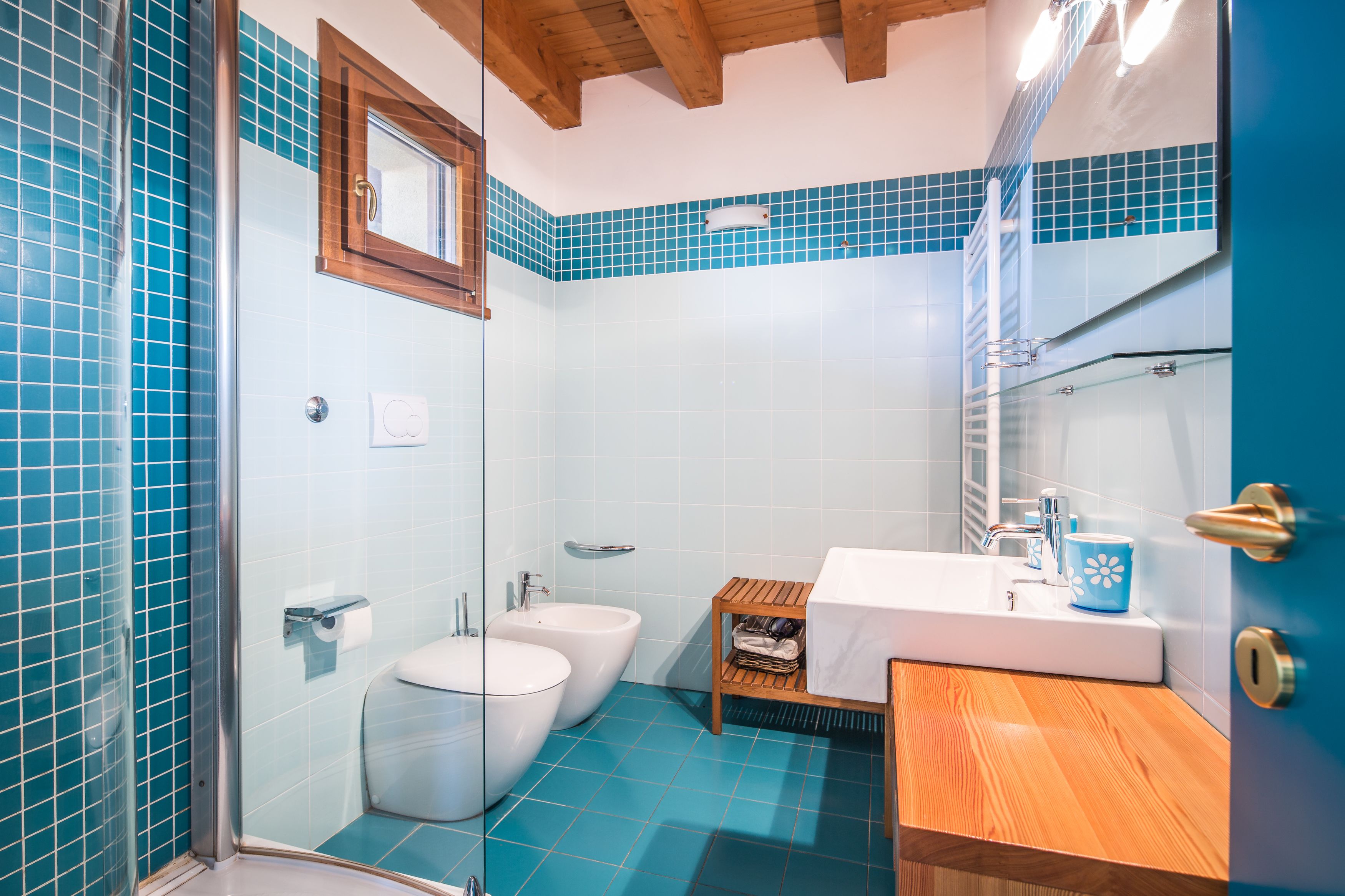 Un baño con cabina de ducha de vidrio, inodoro, bidé, lavamanos con encimera de madera y espejo sobre el lavamanos.