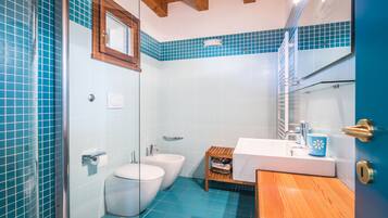 Un baño con cabina de ducha de vidrio, inodoro, bidé, lavamanos con encimera de madera y espejo sobre el lavamanos.