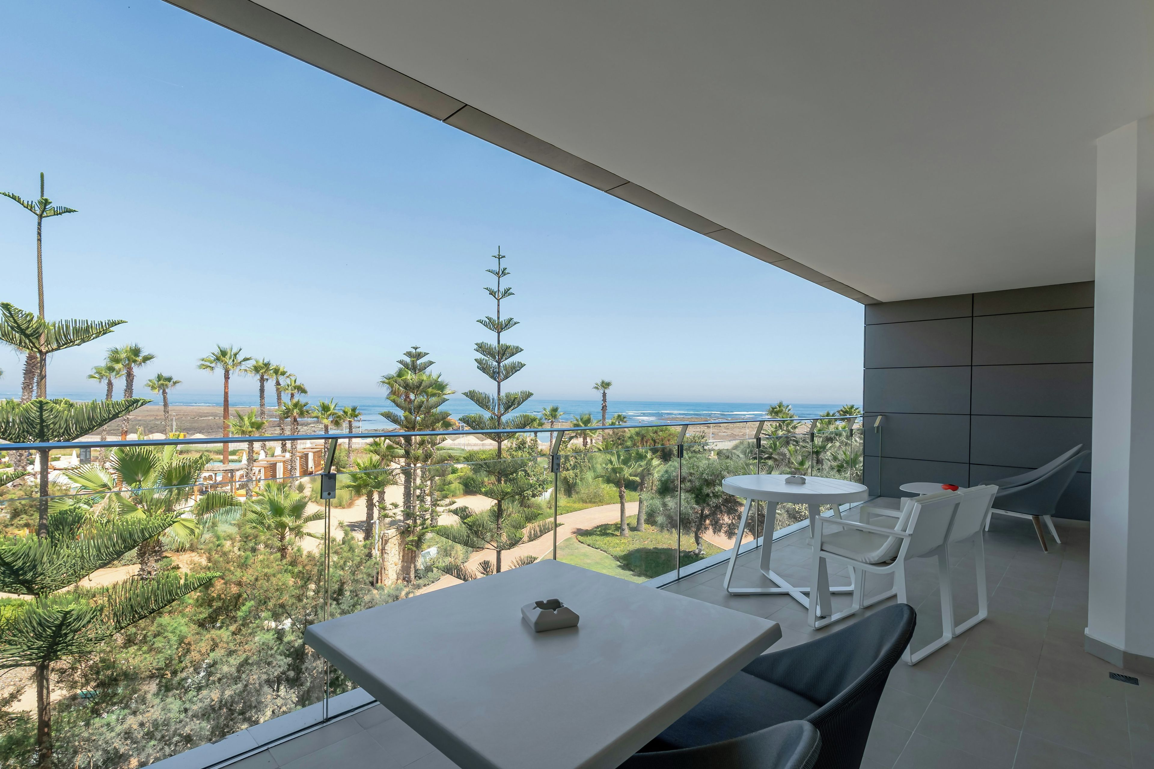 A balcony with a table and chairs, overlooking a beach and ocean.
