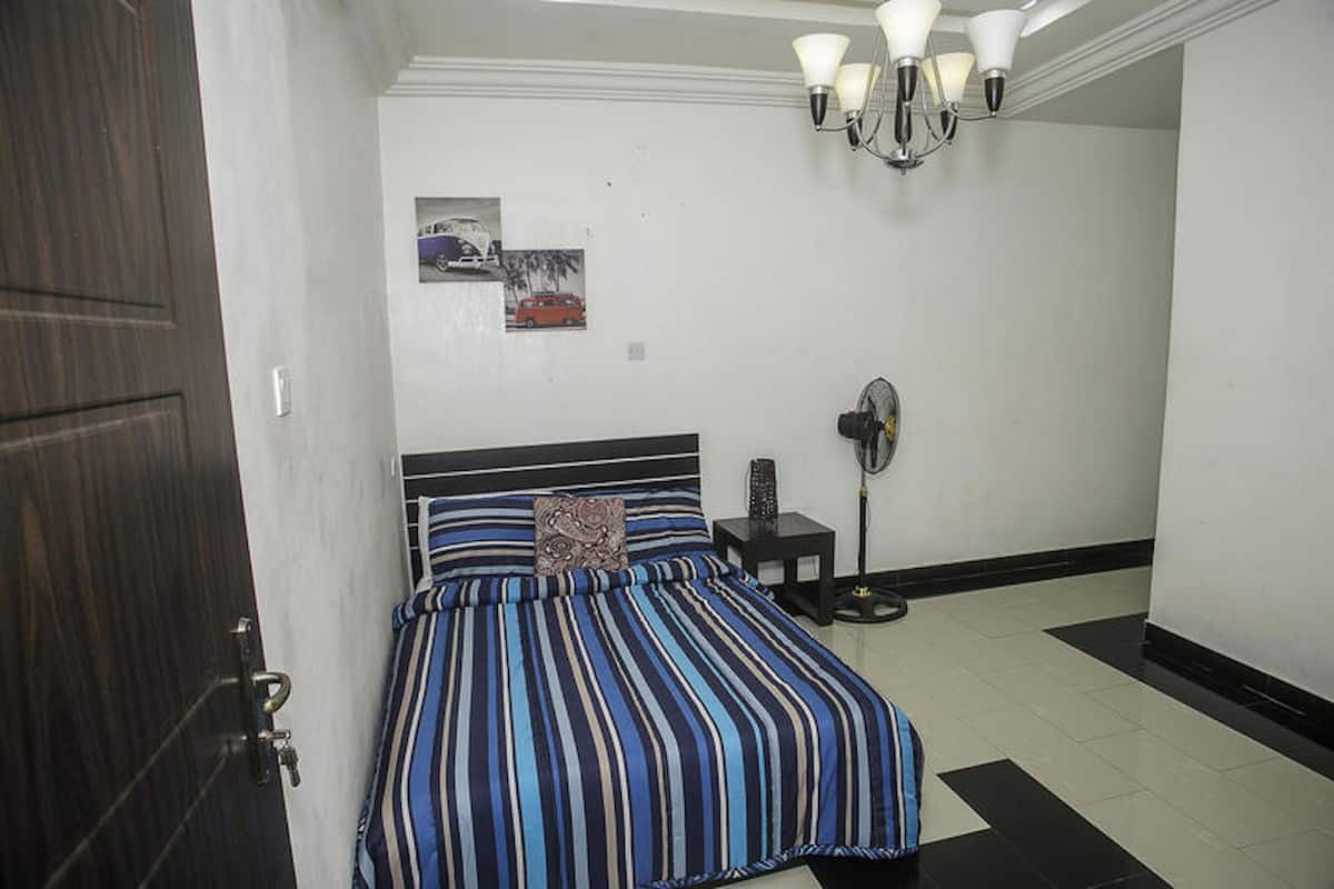 A bedroom with a bed, a bedside table, a wall-mounted fan, and a door.