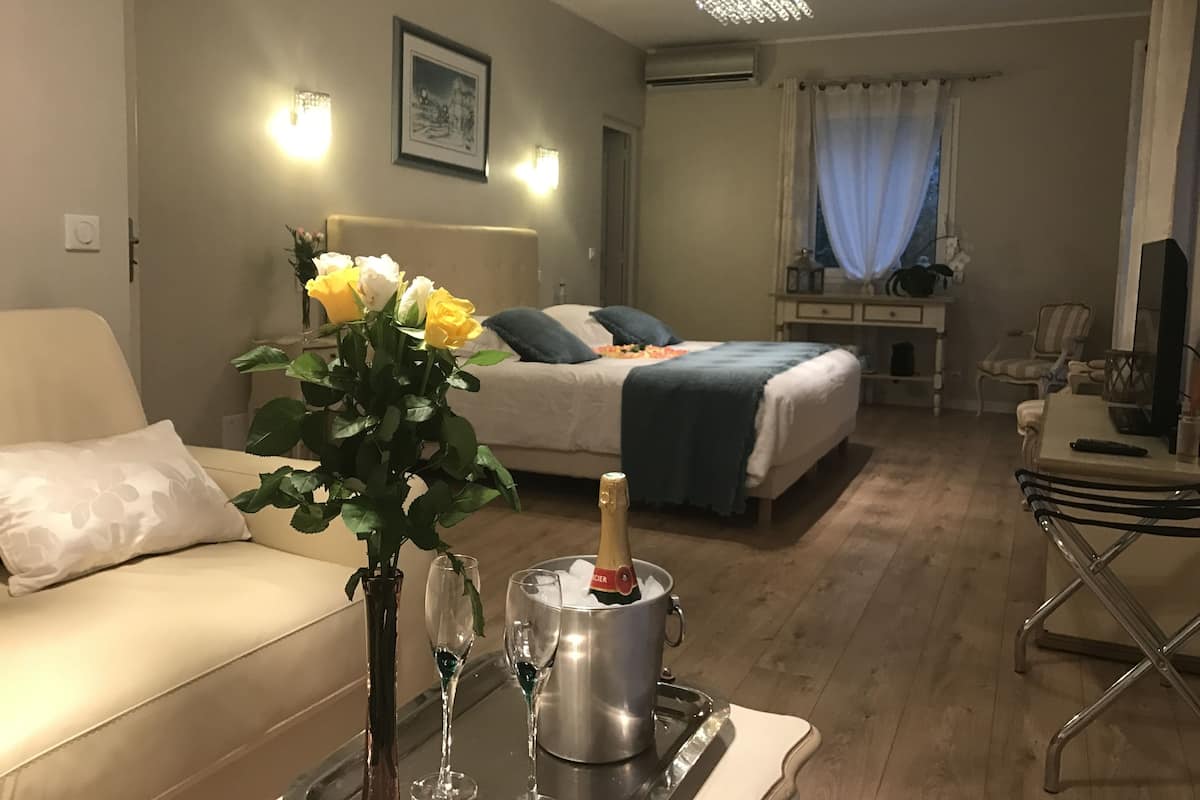 A hotel room with a bed, a bedside table with a vase of flowers, two champagne flutes, and a bottle of champagne.
