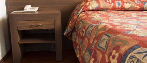 A wooden bedside table with a telephone and a drawer.
