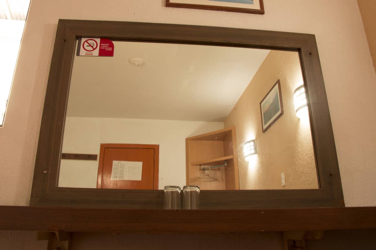 Uno specchio riflette una stanza con una porta in legno, uno scaffale in legno e un quadro appeso al muro.