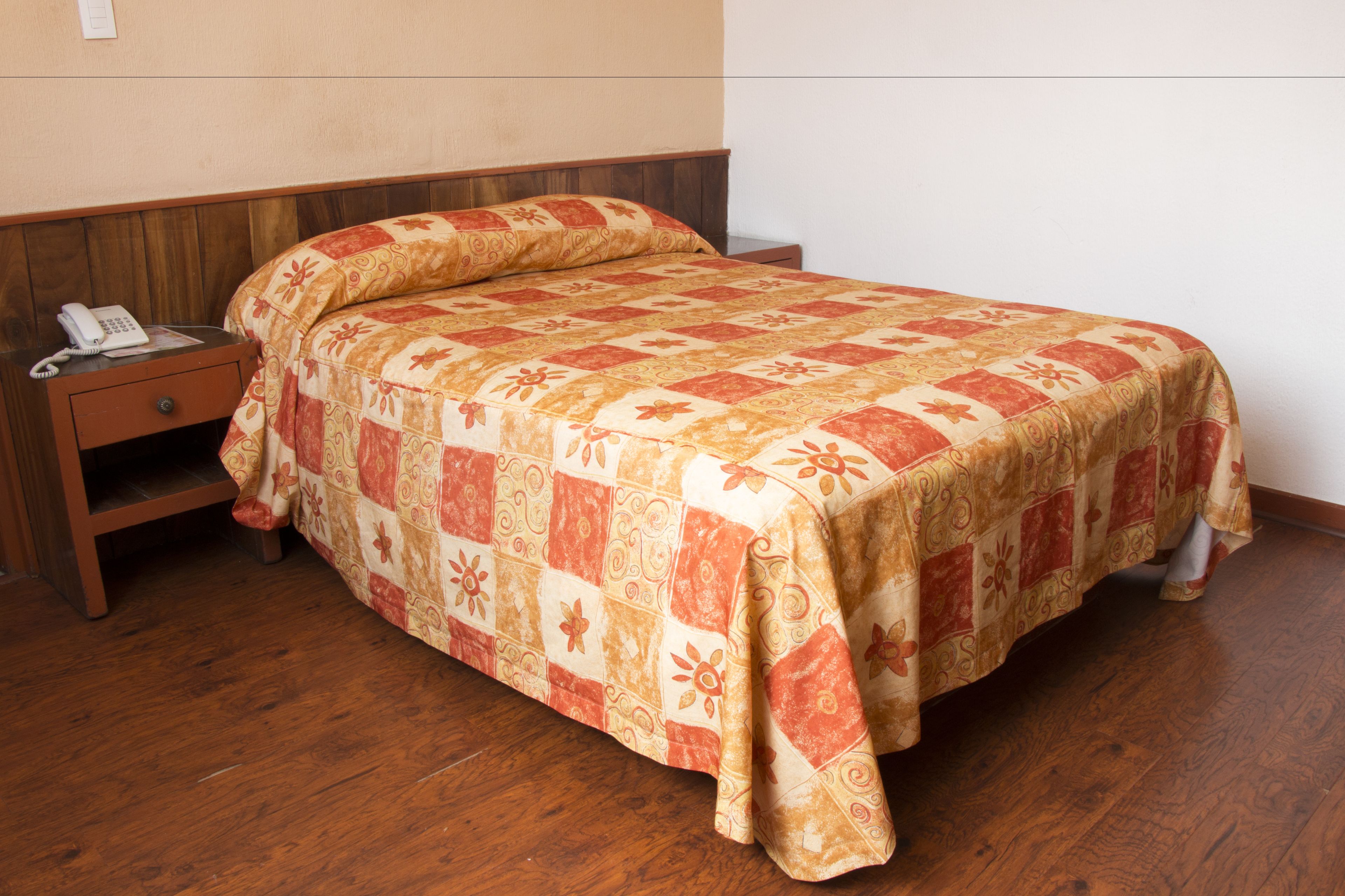 A single bed with a floral quilt, a bedside table with a phone, and a wooden nightstand.