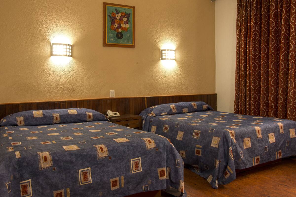 Una camera d'albergo con due letti, un comodino, un telefono e un quadro appeso al muro.