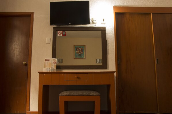 Une pièce avec un bureau en bois, un téléviseur fixé au mur au-dessus, et une porte sur le côté gauche.