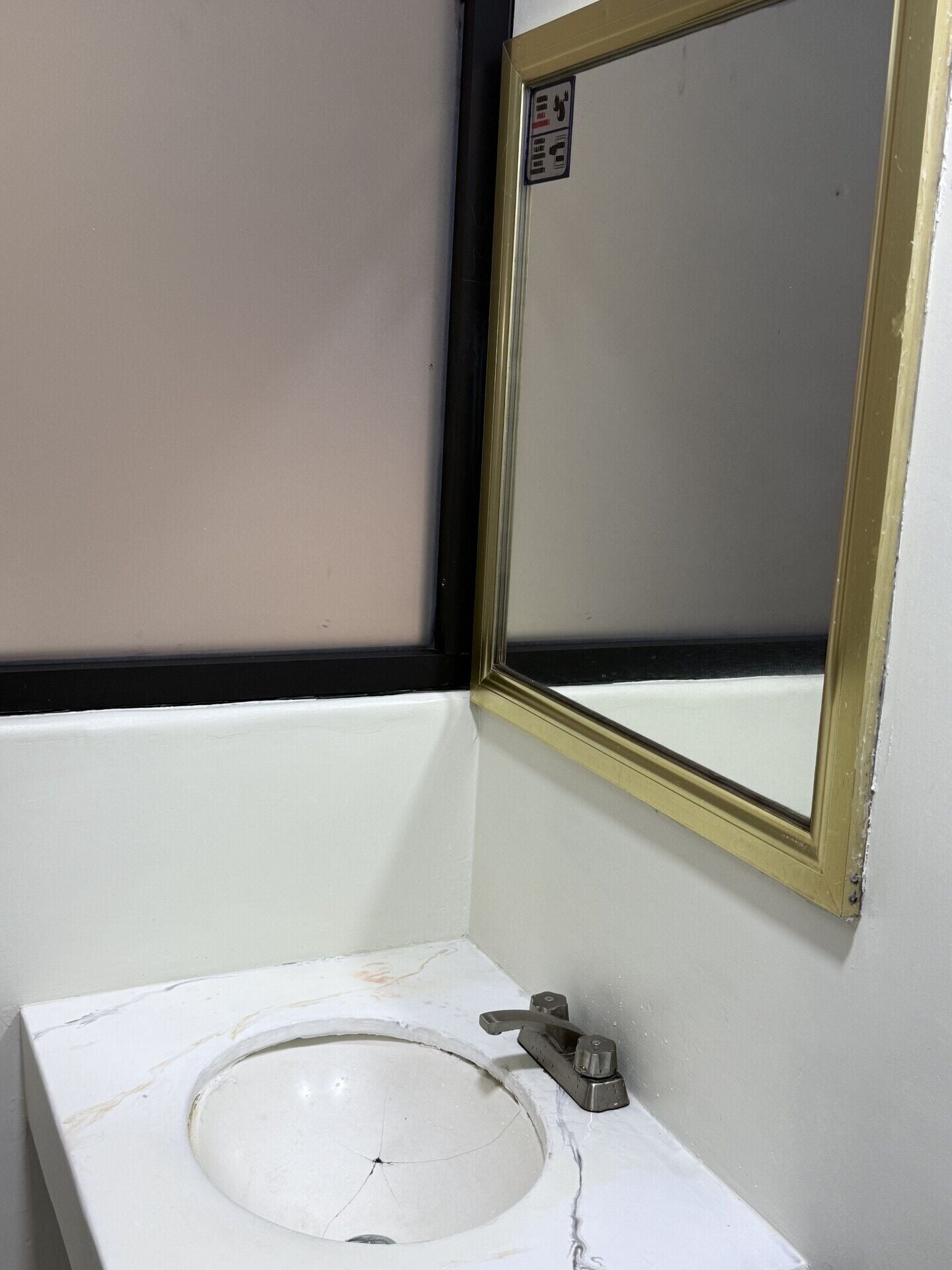 Ein Badezimmer mit einem weißen Waschbecken, einem Spiegel mit goldener Rahmung und einem schwarzen Fensterrahmen.