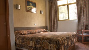 A bedroom with a bed, a chair, a window with curtains, and a painting on the wall. - Hotel El Estadio (Mexico City)