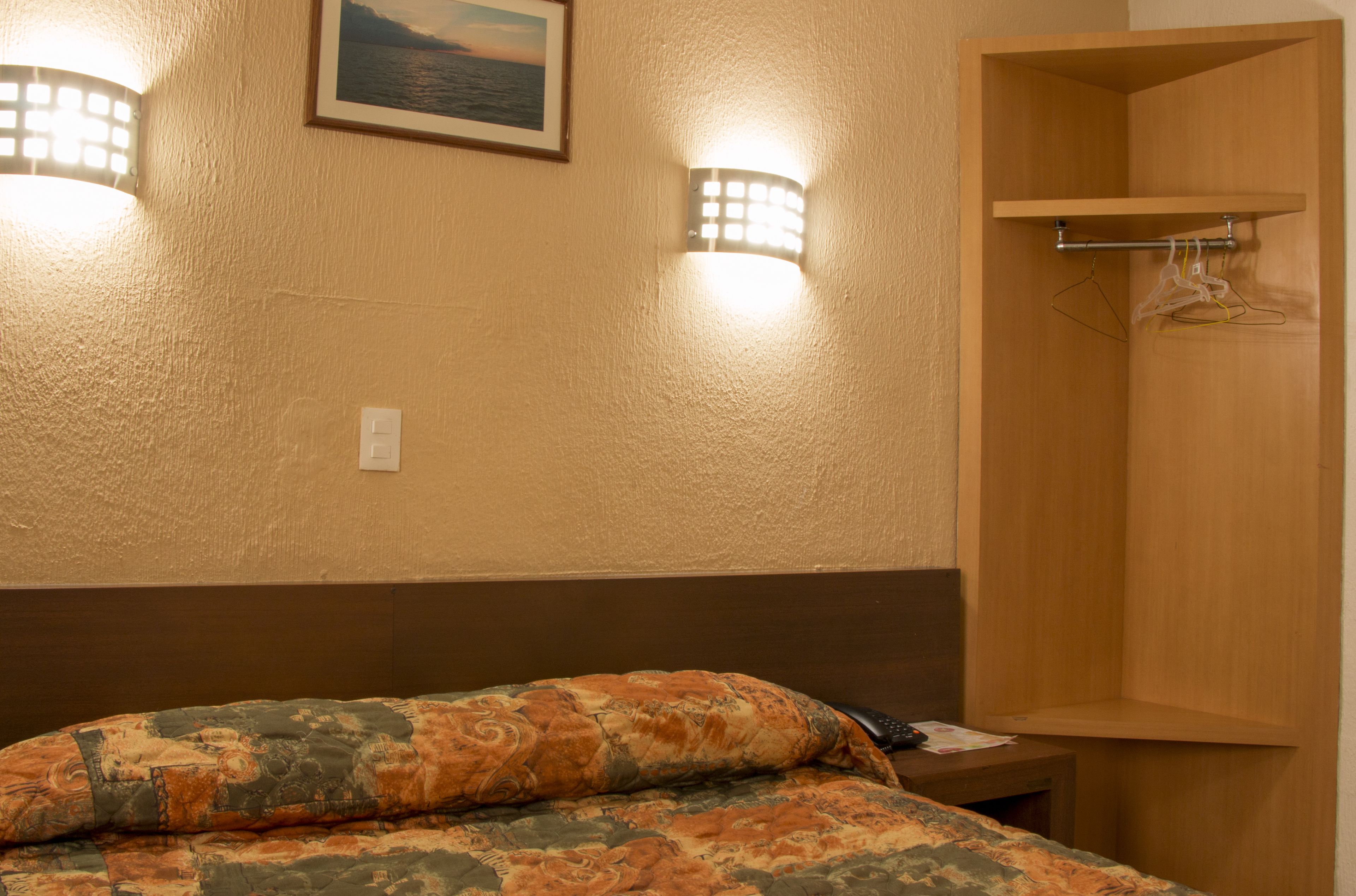 A hotel room with a bed, a wooden wardrobe, and wall-mounted lights.