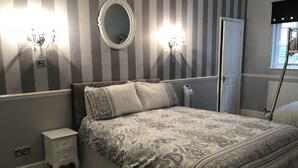 Un dormitorio con cama, mesita de noche, espejo en la pared y dos apliques.