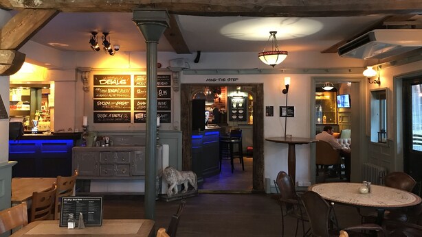 Interior acogedor de restaurante con vigas de madera, una zona de bar y una distribución de mesas.