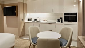 Une cuisine moderne avec des meubles blancs, un four encastré et un coin repas équipé de deux chaises.