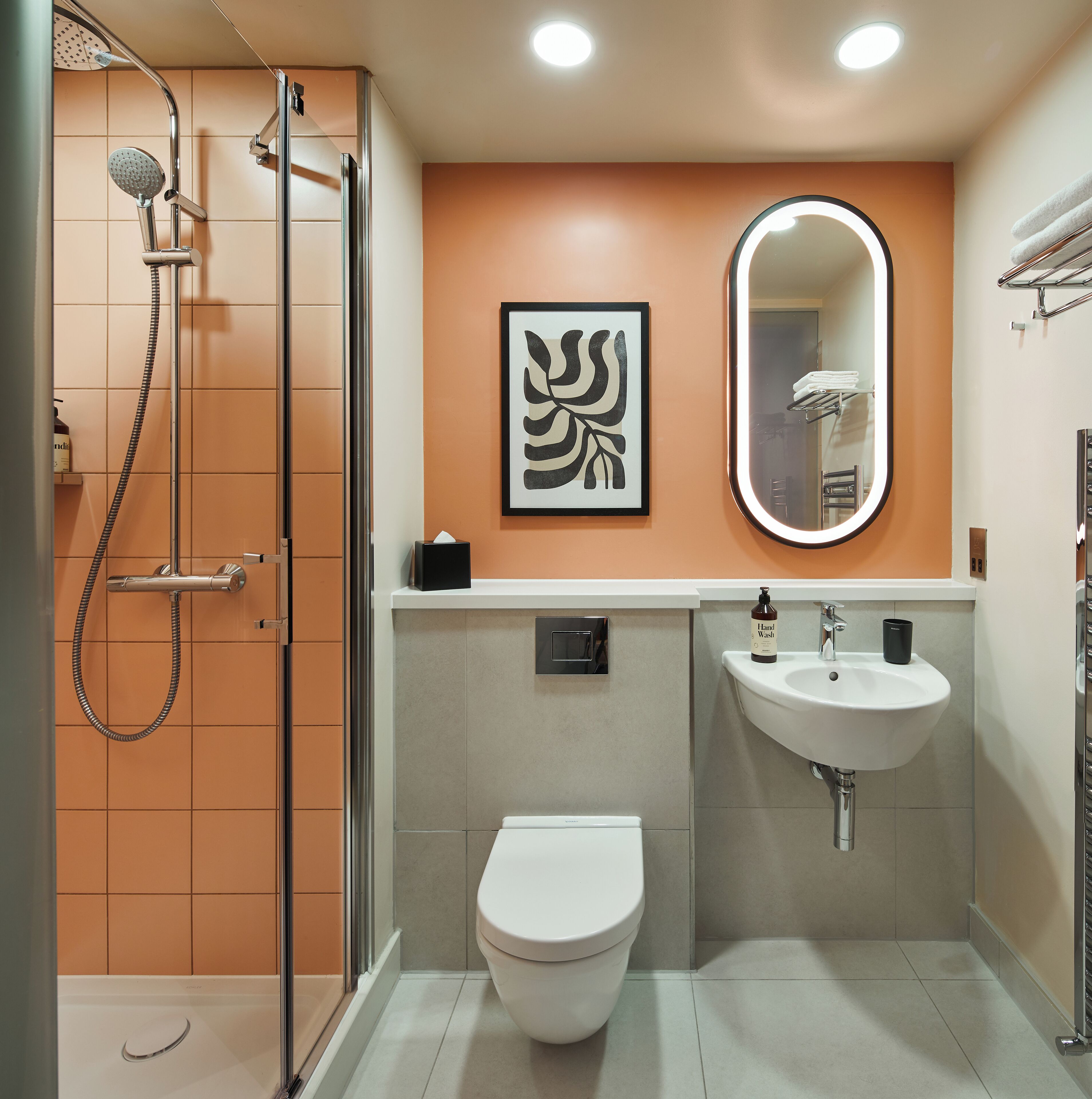 A modern bathroom with a glass-enclosed shower, a white toilet, a sink with a mirror, and a framed artwork on the wall.