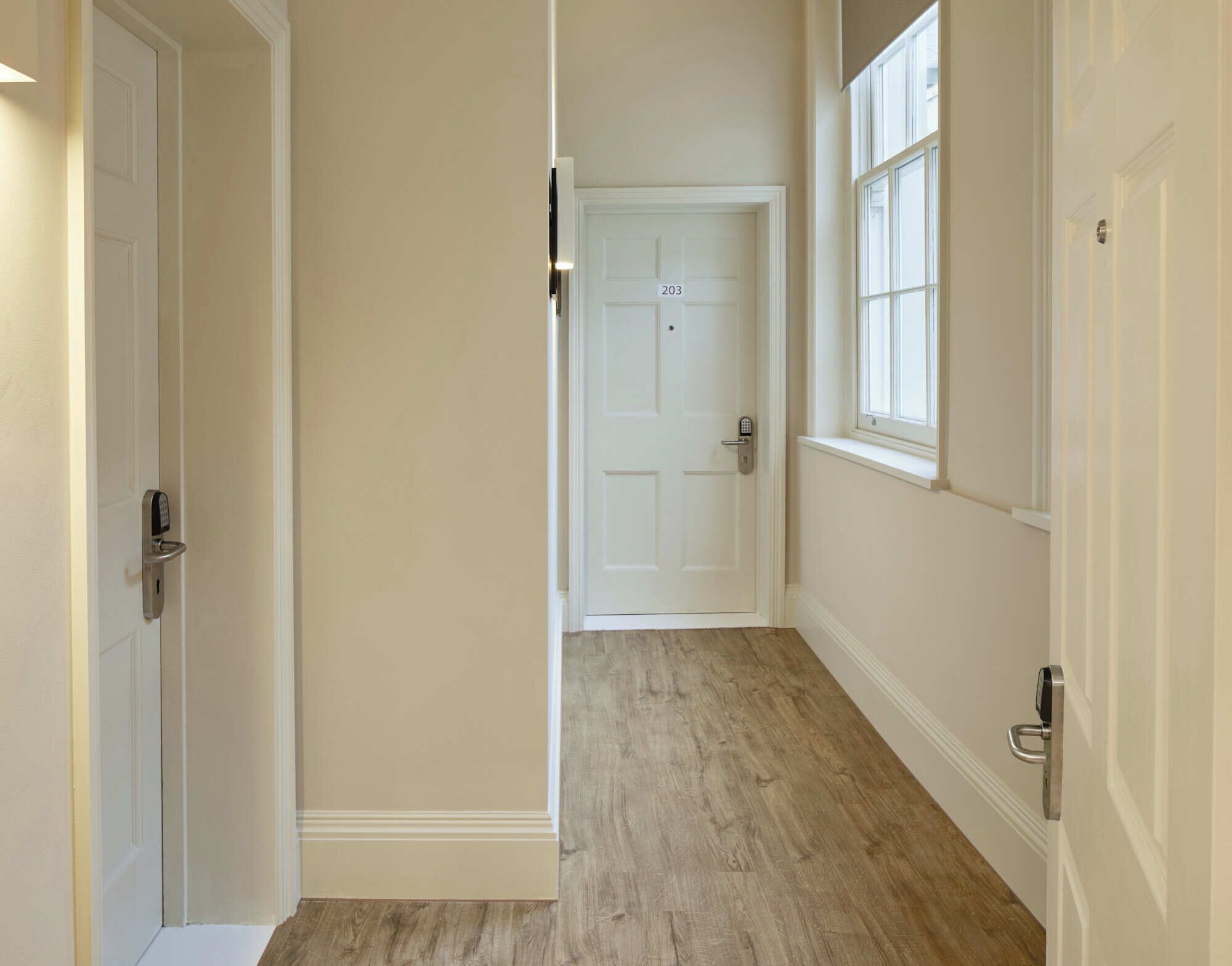 A hallway with a wooden floor, white walls, and a door marked with the number 203.