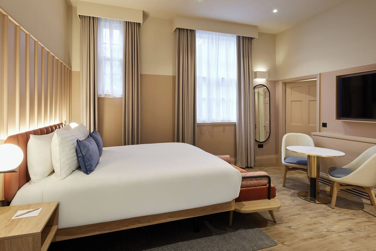 Une chambre d’hôtel avec un grand lit, un bureau, une chaise, une table ronde et un téléviseur.