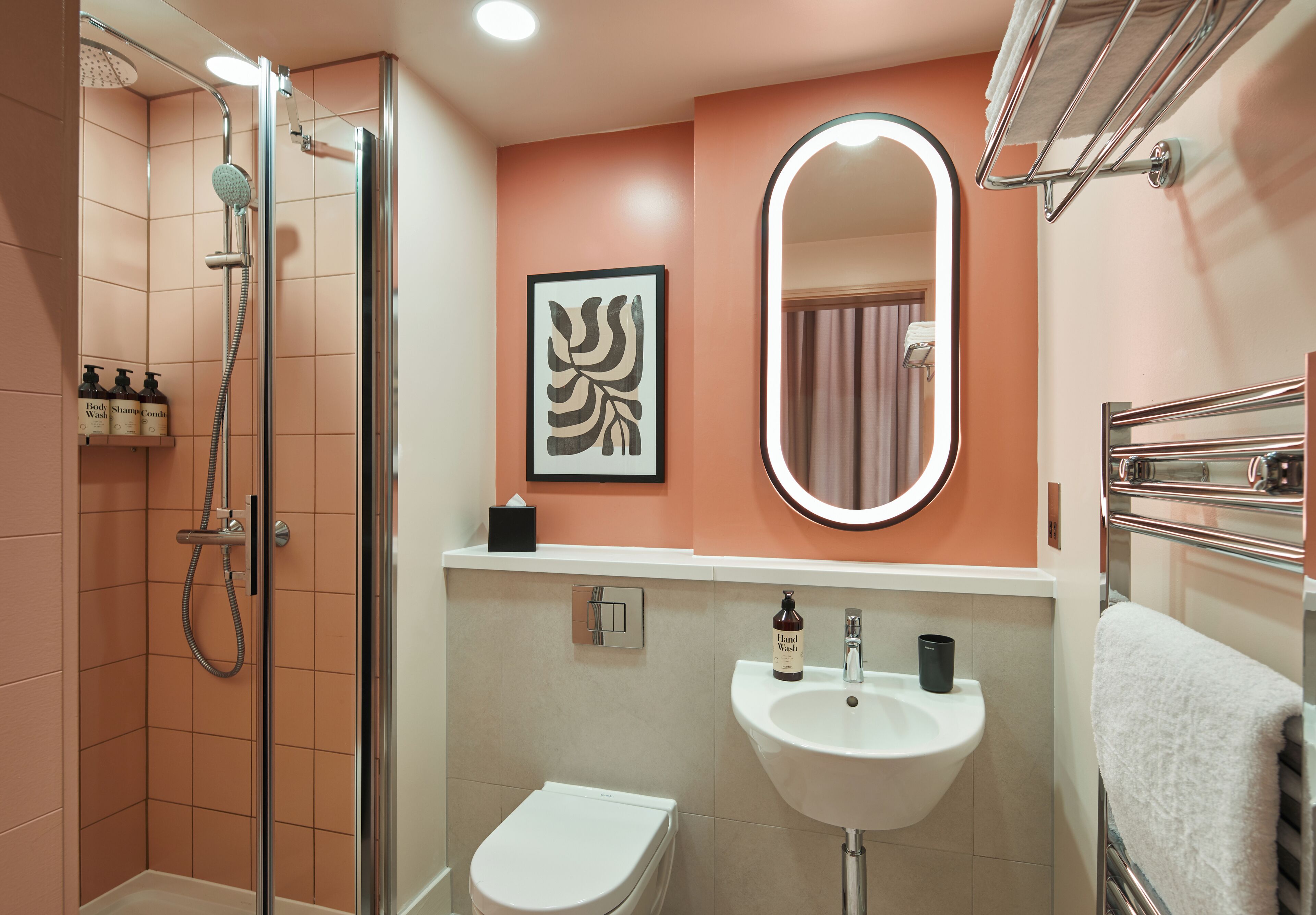 Une salle de bain avec une douche à parois de verre, un lavabo blanc et un miroir doté d’un cadre éclairé.