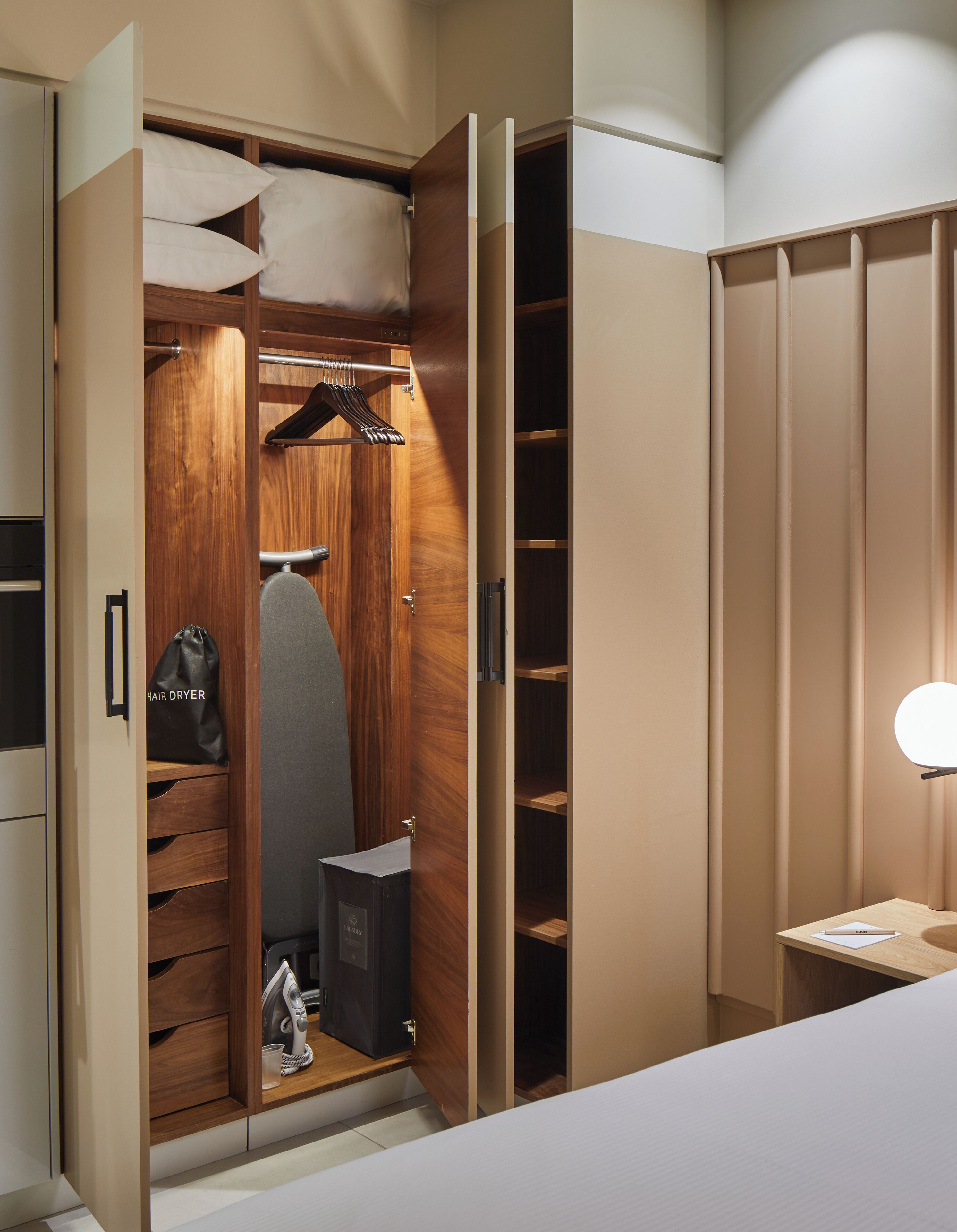 A walk-in closet with wooden shelving, a hanging rack, and a hair dryer bag.
