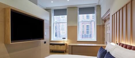 A modern bedroom with a large bed, a TV mounted on the wall, and a window with a view of buildings.