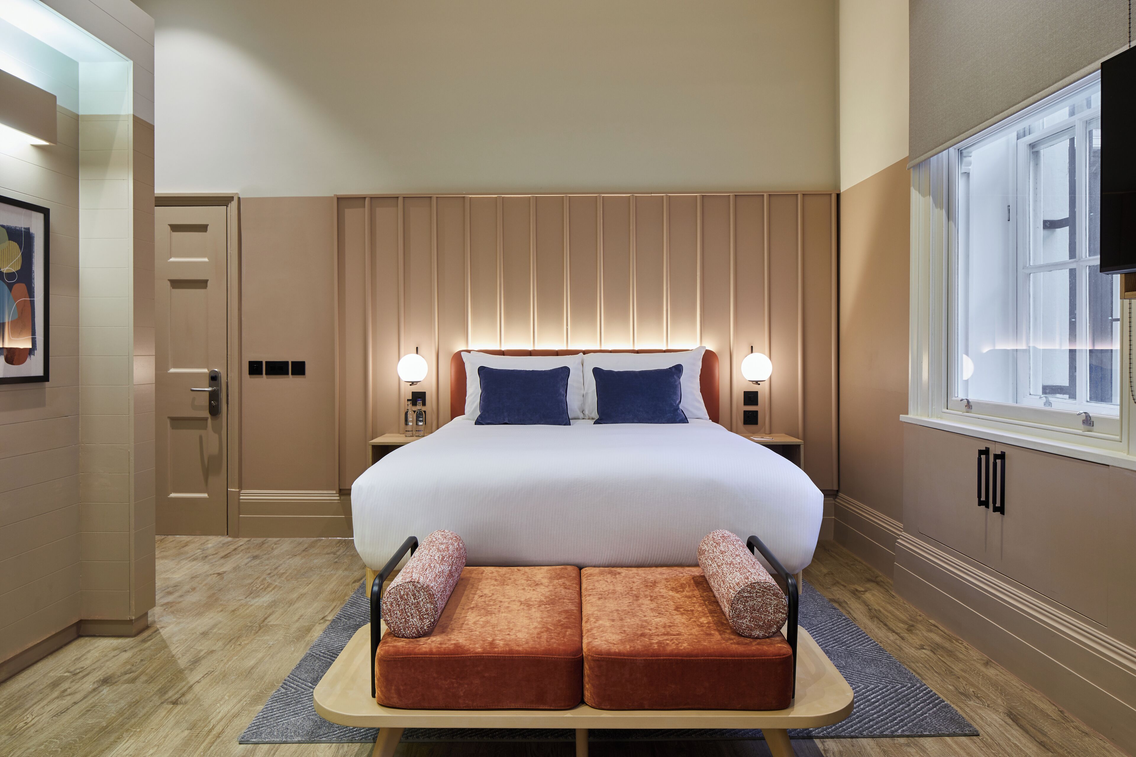 A hotel room with a large bed, bedside lamps, a window, and a door.
