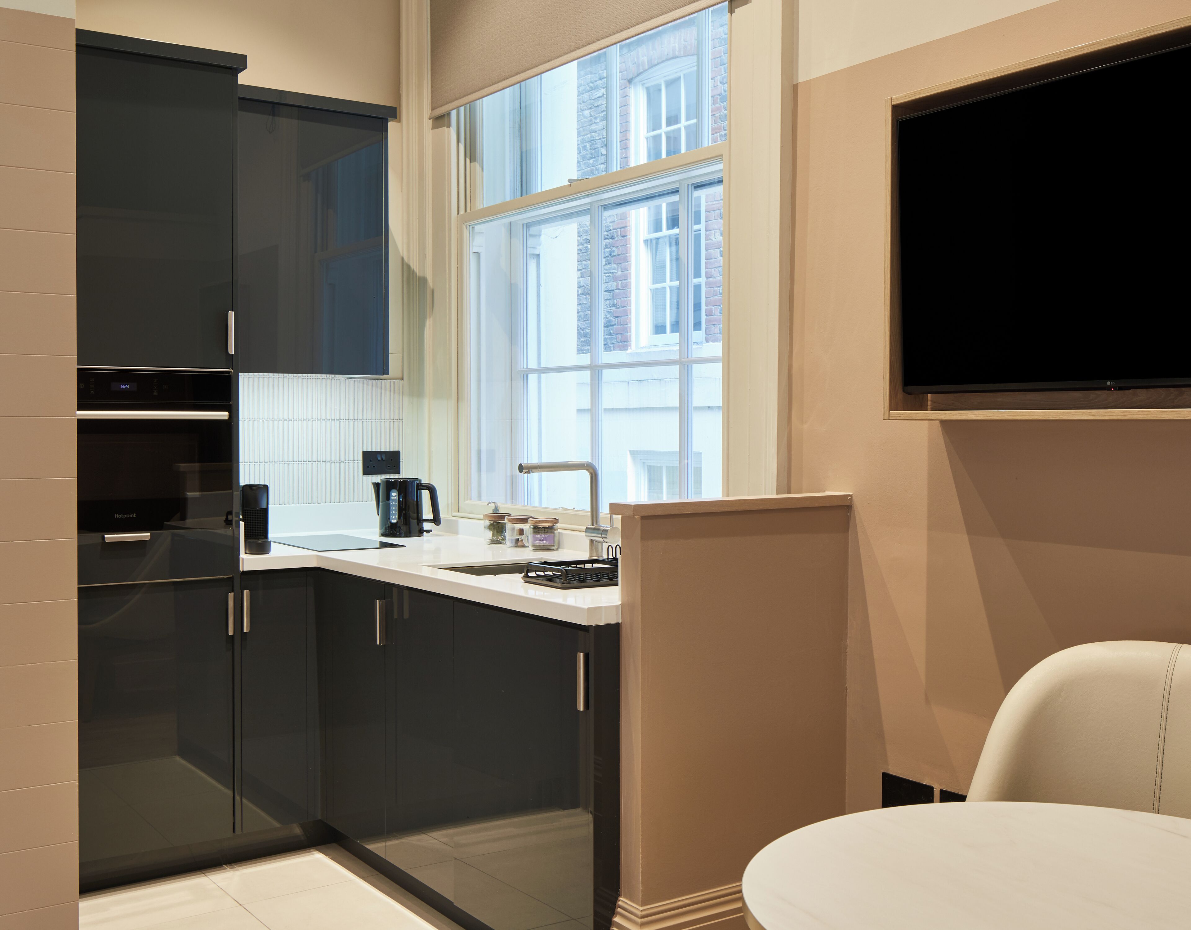 A modern kitchen with dark cabinets, a built-in oven, a coffee maker, and a window with a view of buildings.