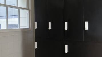 A room with a large black wardrobe, a window with blinds, and a tiled floor.
