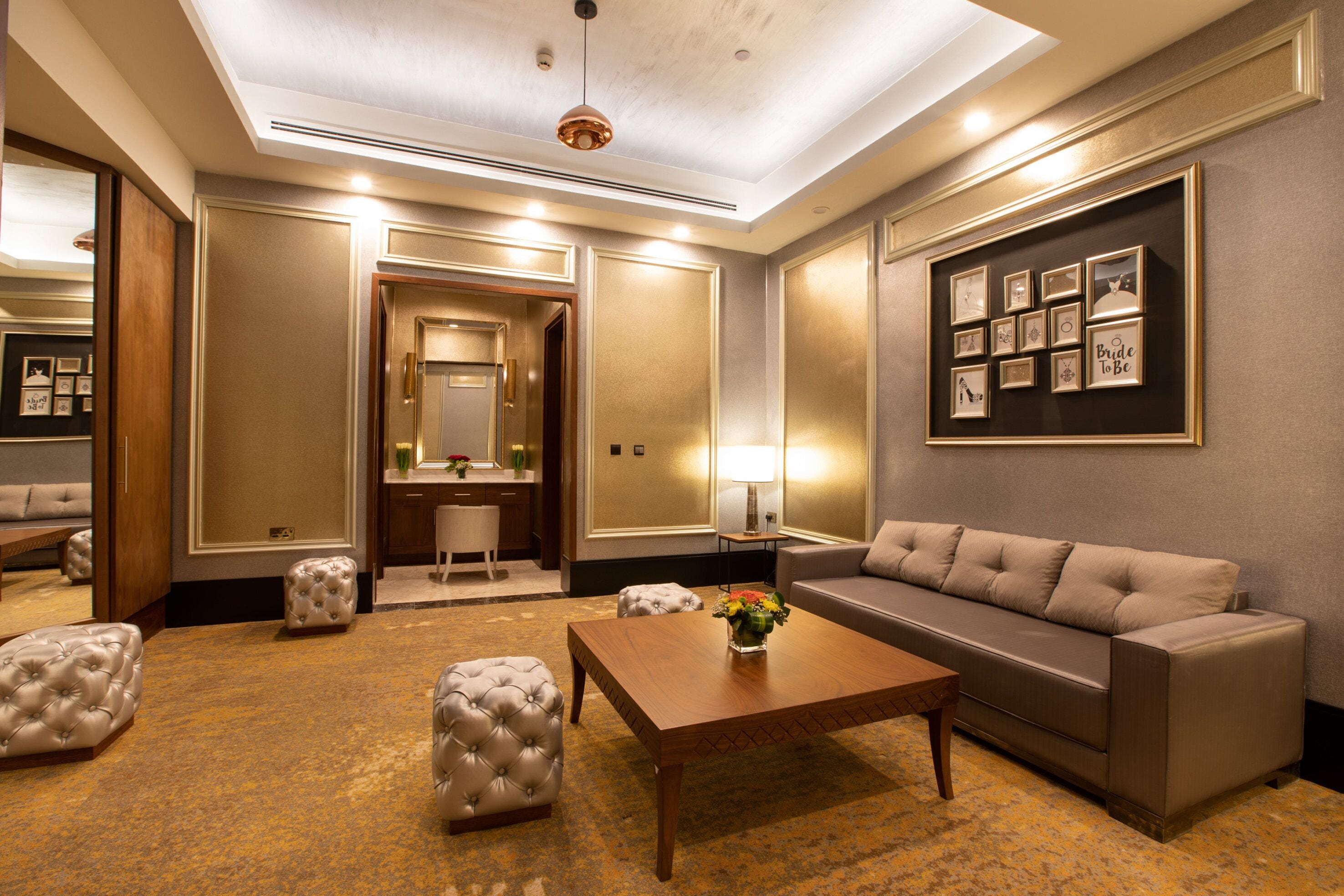 Un salon bien éclairé et élégamment aménagé, avec un canapé, des poufs, une table basse et des tableaux encadrés accrochés au mur.