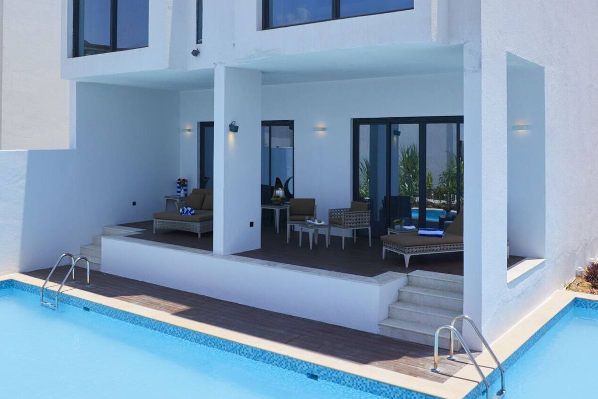 Una casa moderna de dos pisos con piscina, ventanas amplias y mobiliario exterior.