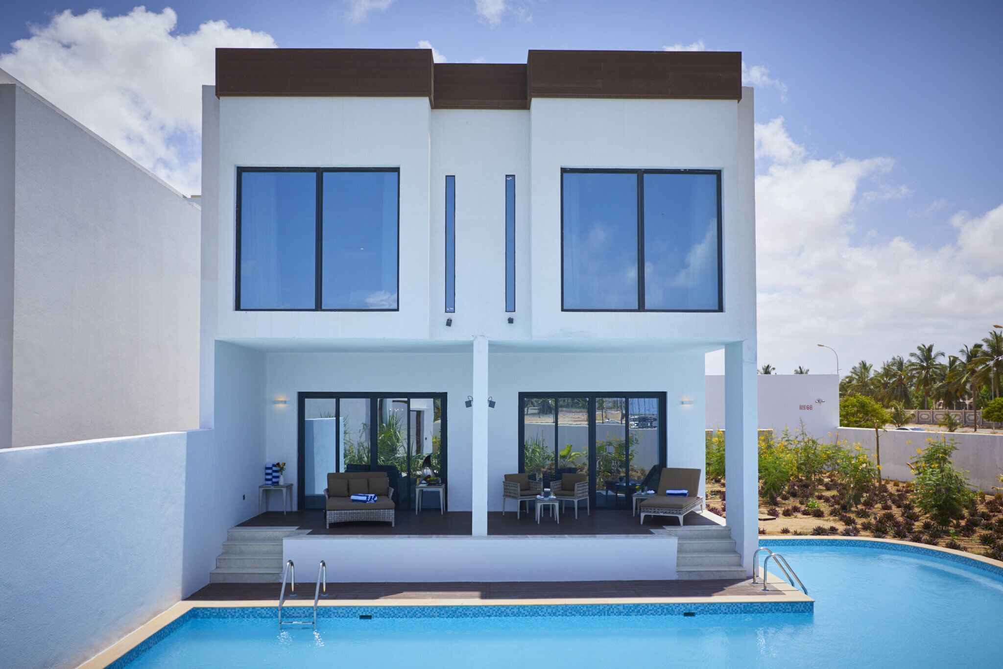 Une maison moderne à deux étages, dotée d’une piscine, de grandes fenêtres et d’un espace extérieur aménagé pour se détendre.