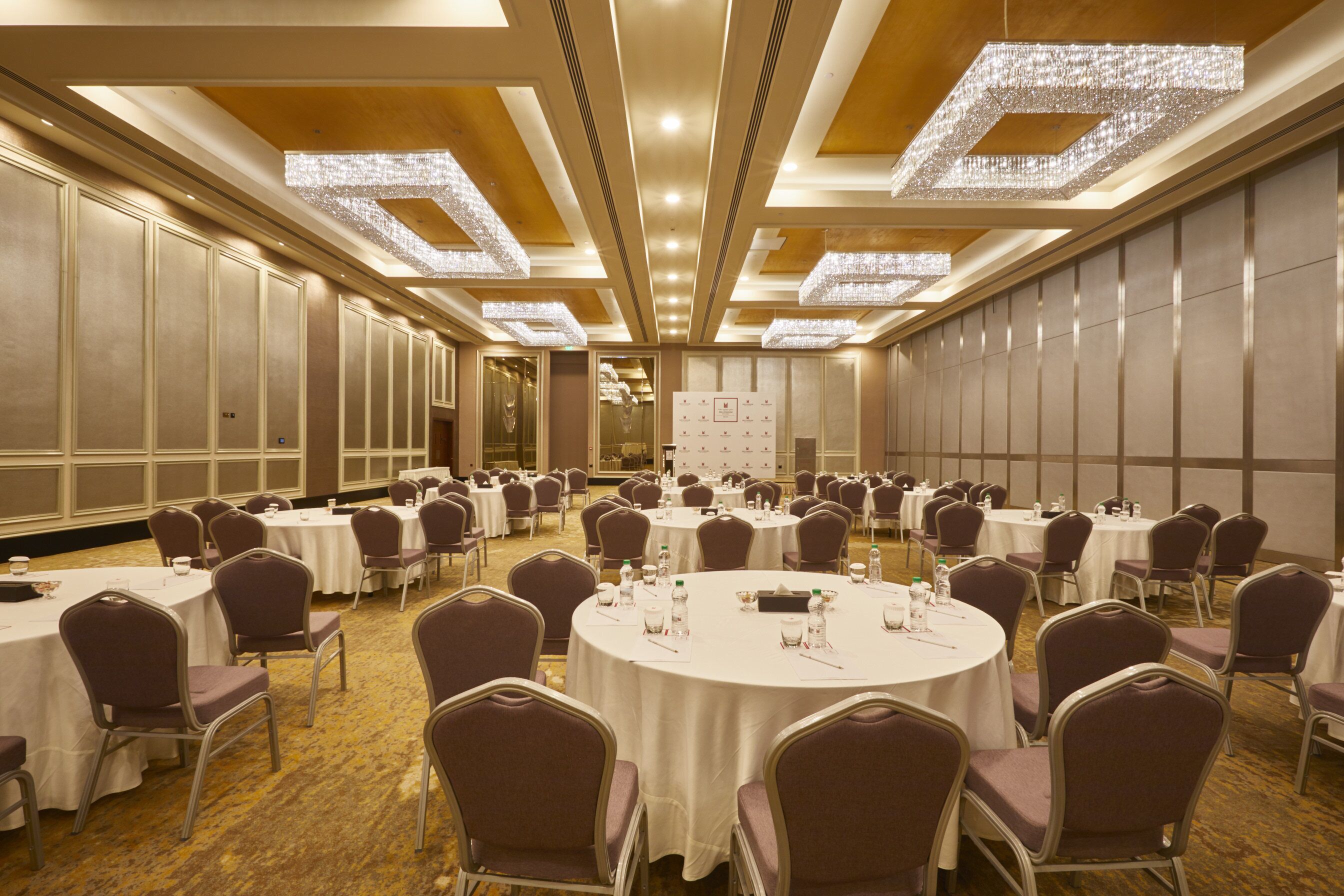 A large conference room with round tables and chairs, equipped with water bottles and nameplates.
