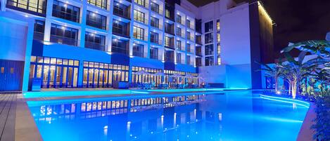 Un hotel moderno con piscina, varios balcones y una fachada bien iluminada.