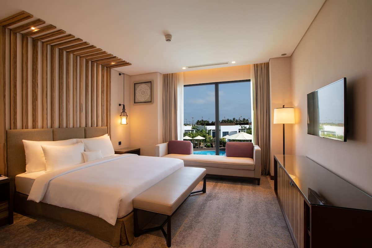 Habitación de hotel con una cama grande, un área de descanso con vistas a la piscina y un televisor de pantalla plana.