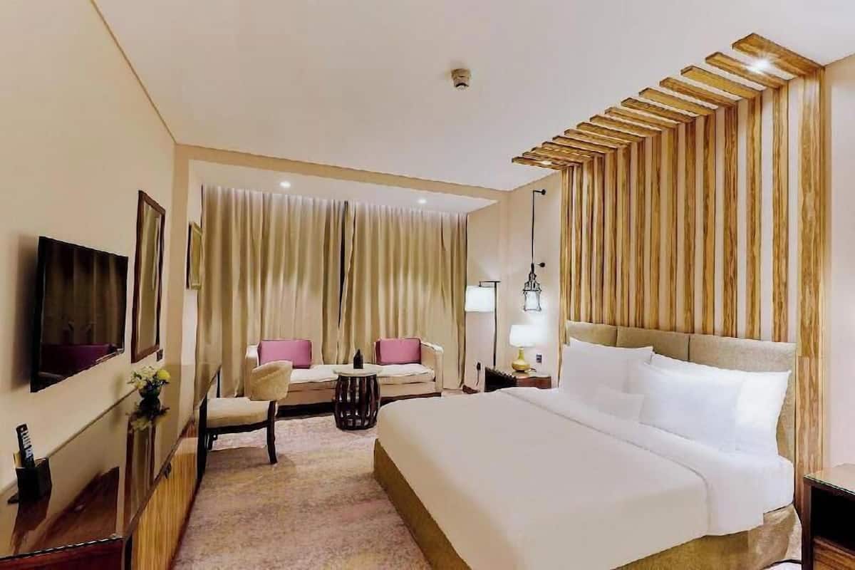 Habitación de hotel con una cama grande, un sofá, un televisor y un escritorio con lámpara.