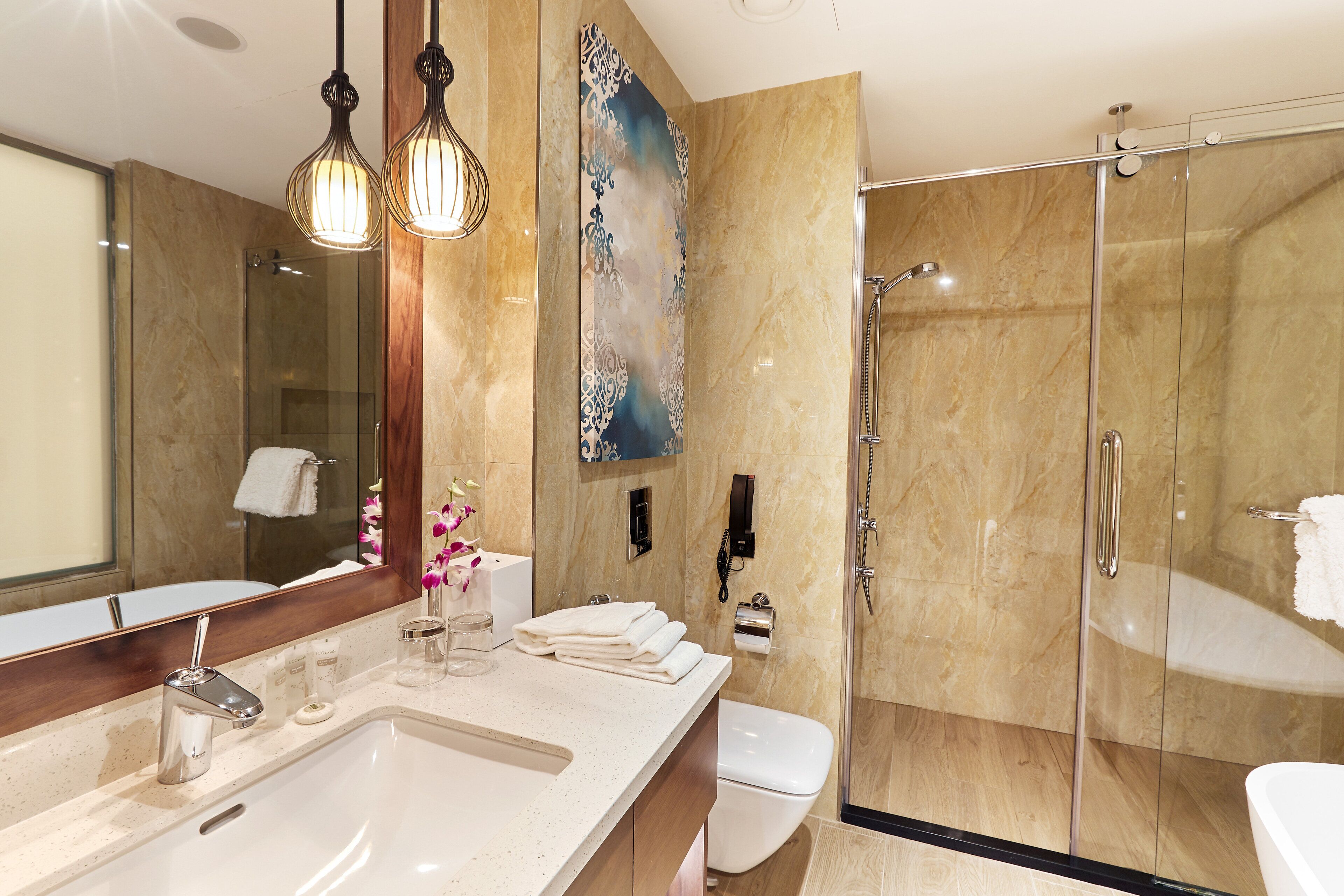 Un baño moderno con un espejo grande, un lavabo, un inodoro y una ducha con mampara de vidrio.