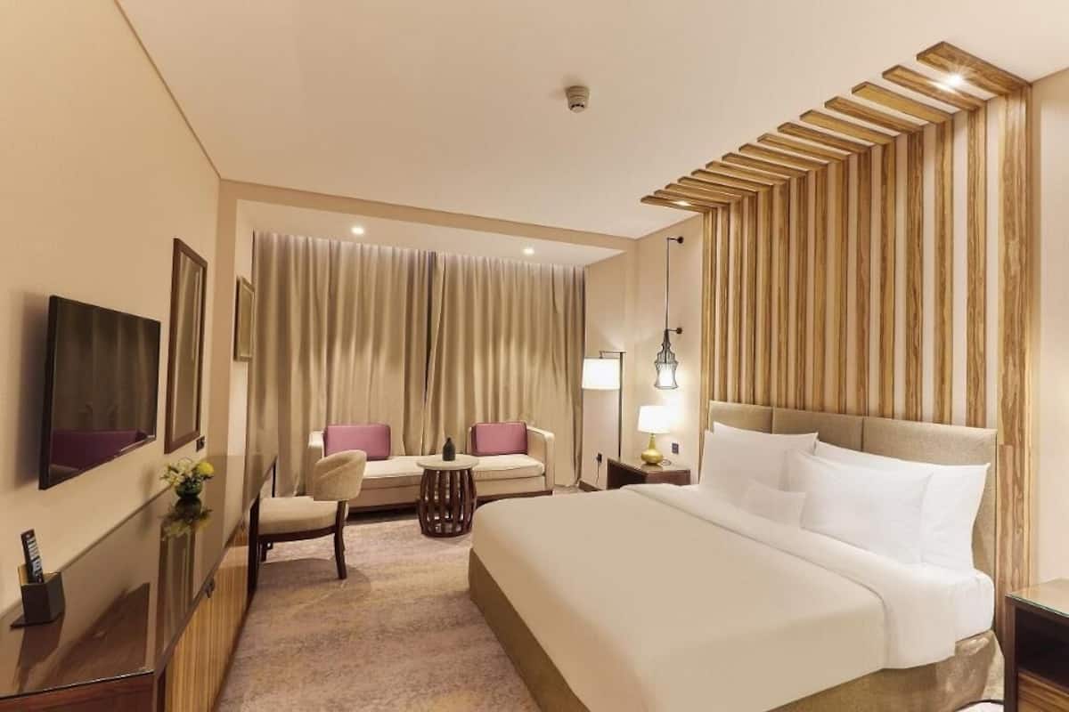Una habitación de hotel con una cama grande, un sofá, un televisor y un escritorio con lámpara.