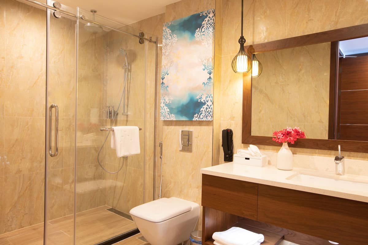 Un baño moderno con cabina de ducha de vidrio, inodoro blanco, tocador con espejo y un florero con flores.