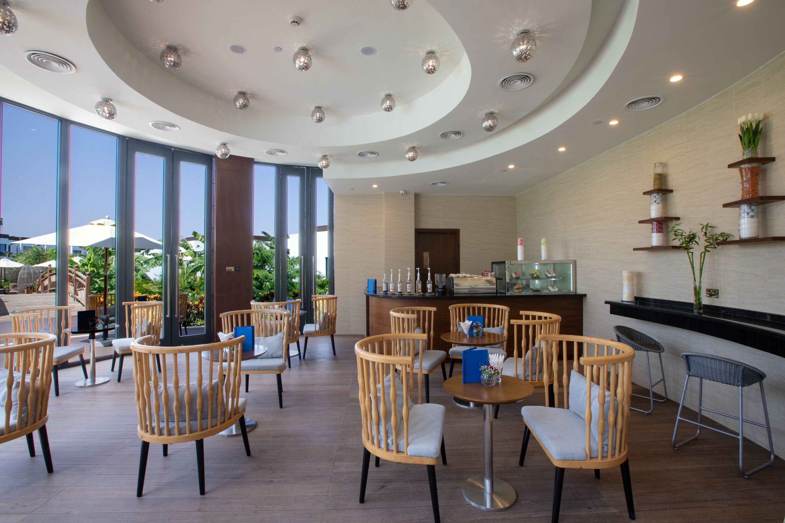 Un moderno comedor interior con sillas y mesas de madera, una barra y grandes ventanales con vistas al exterior.