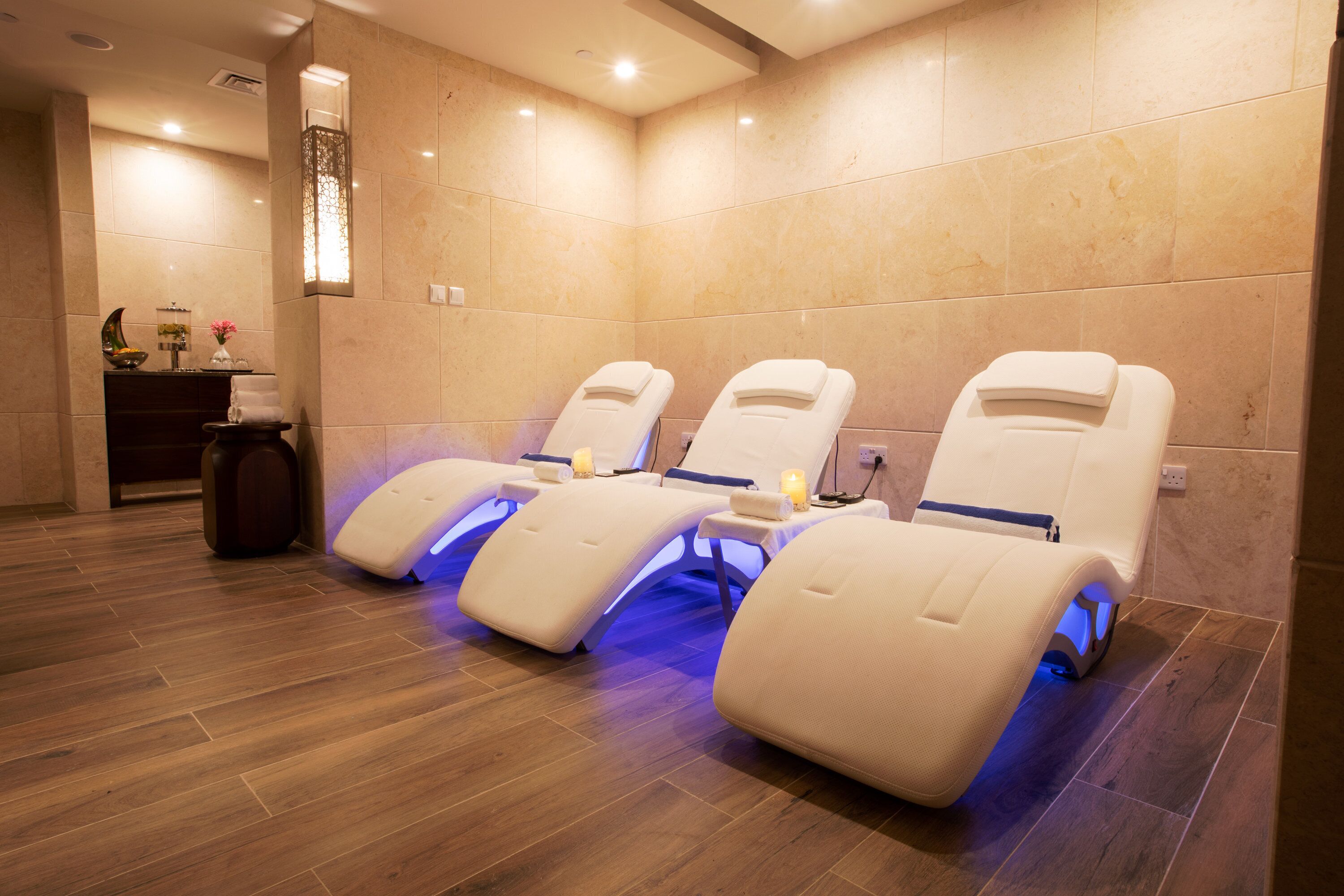 A spa room with three massage chairs, a small table with a candle, and a decorative wall piece.