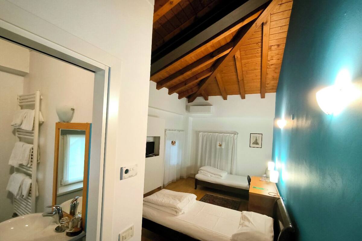 A bedroom with a wooden ceiling, a bed, a bedside table with a lamp, and a bathroom with a sink and towel rack.