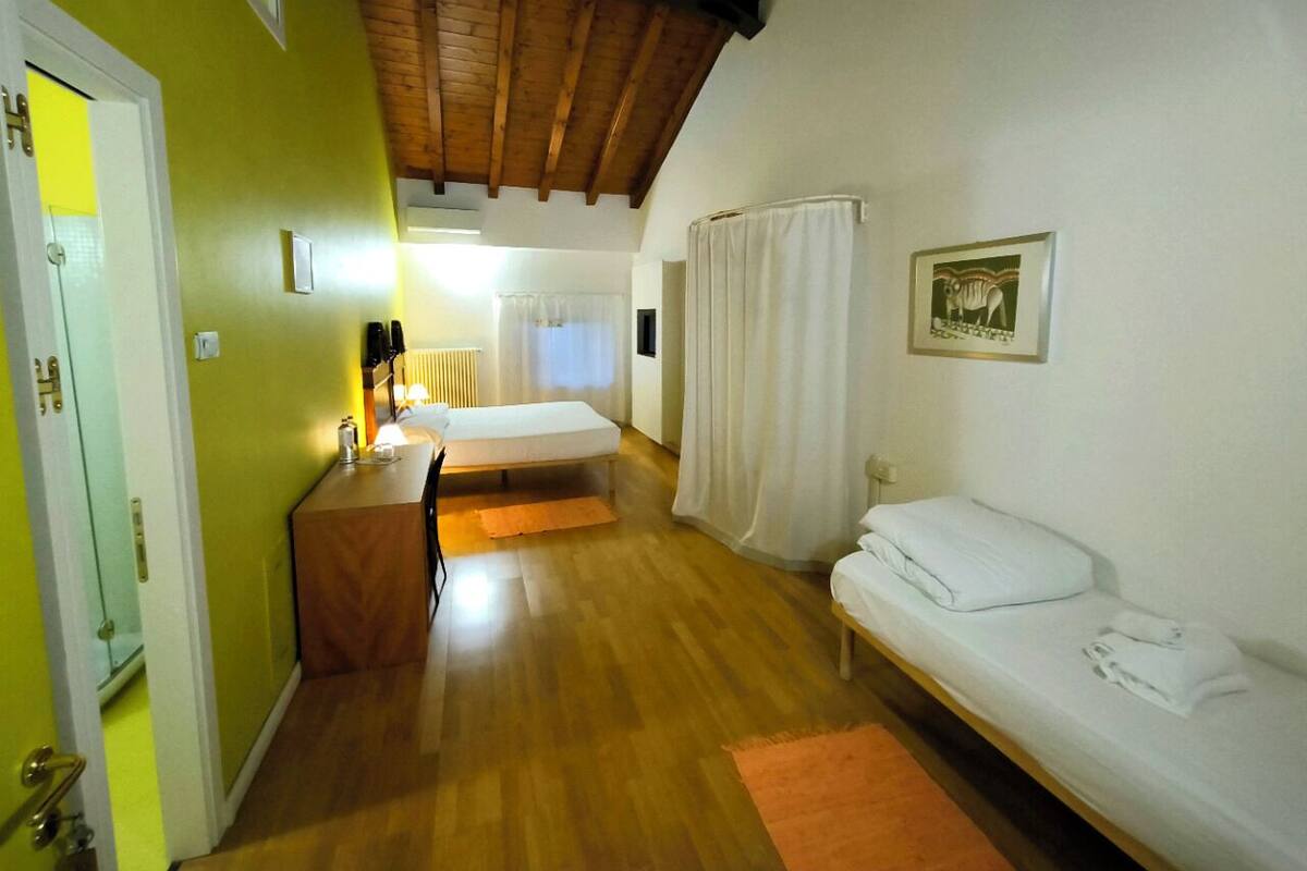 A room with a wooden ceiling, a bed, a bench, a small table, and a door.
