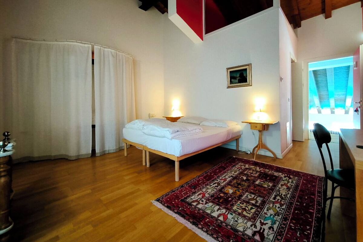 A bedroom with a bed, bedside tables, a rug, and a view of the outside.