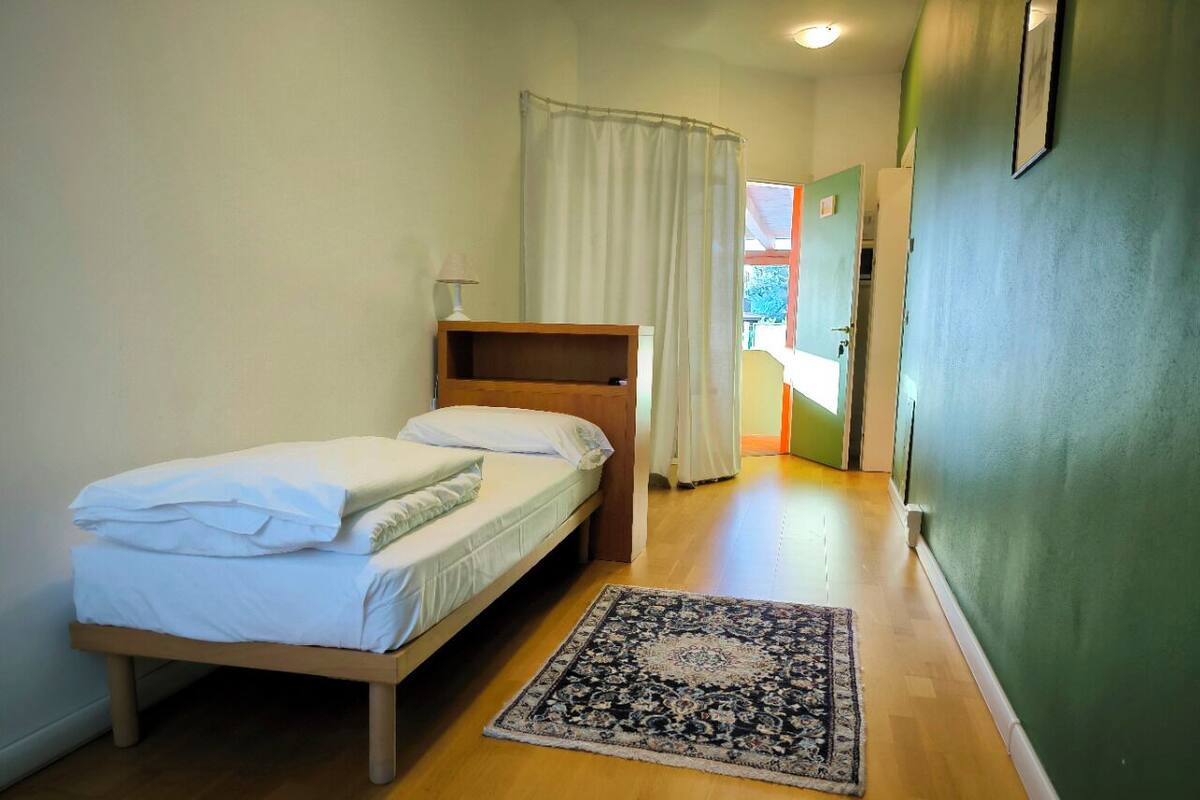 A bedroom with a bed, a bedside table, a rug, and a view of the outside.